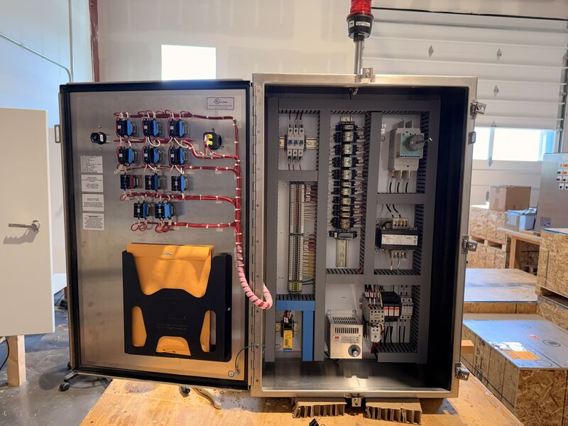 Open stainless steel control panel with relays and labeled wiring on the inside of the door, a document pocket, and a subpanel with breakers, terminal blocks and a disconnect switch.