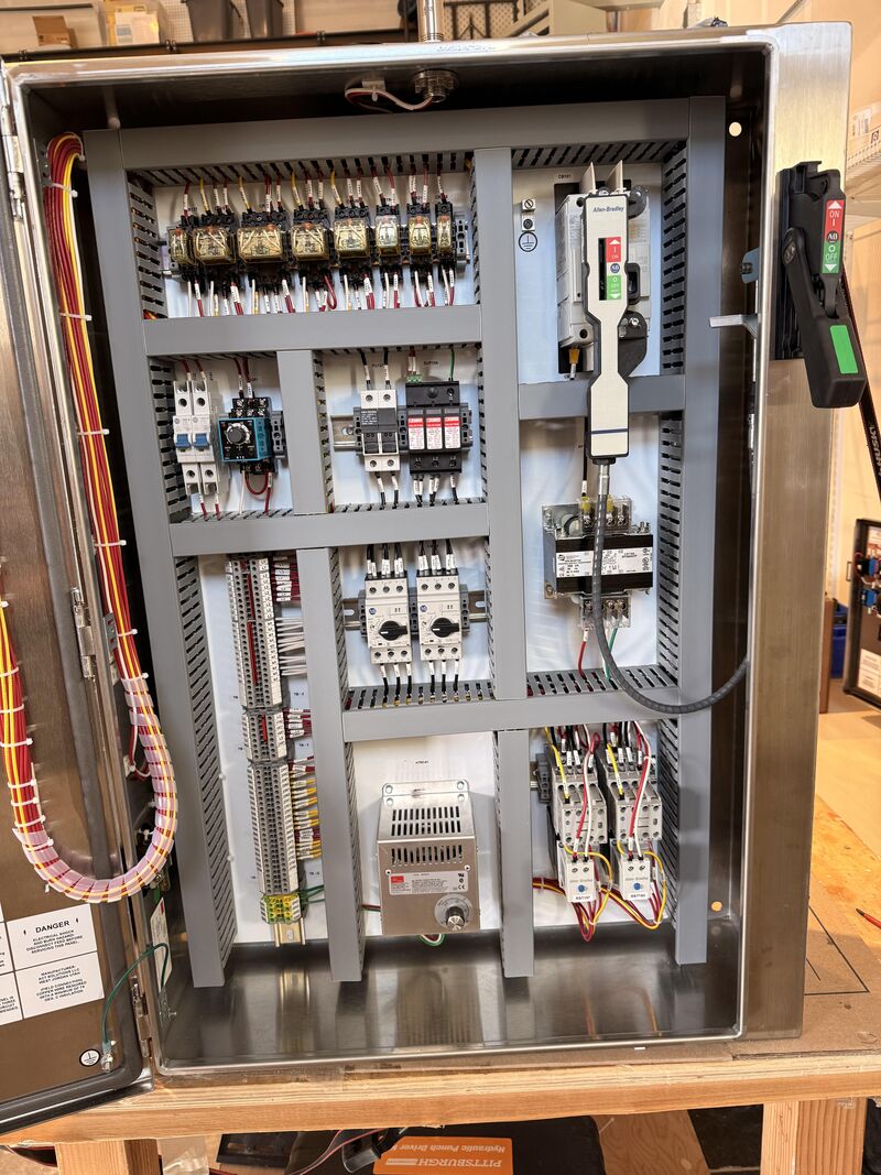 Control panel subpanel with a bank of relays across the top, circuit breakers and contactors in the middle, terminal blocks down the left side, and a power supply and control transformer at the bottom.