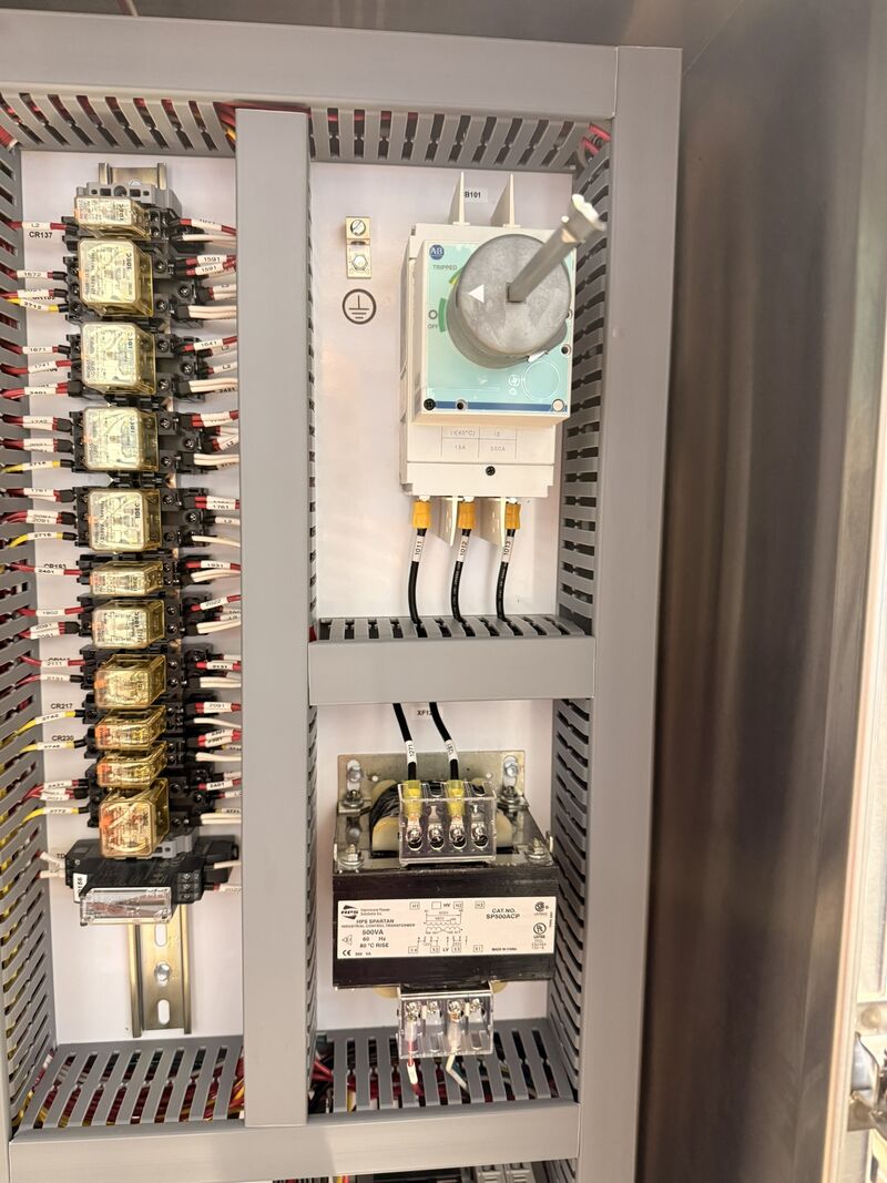 Close-up of a control panel interior showing a row of DIN-rail mounted relays with individually numbered wire labels, a rotary disconnect switch, and a control transformer below.